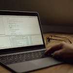 Person working on programming code on a laptop indoors. Glasses on the table.