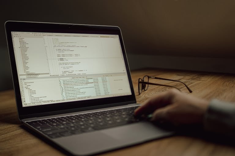 Person working on programming code on a laptop indoors. Glasses on the table.